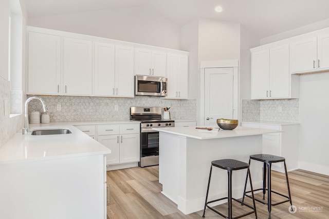 kitchen with a kitchen breakfast bar, stainless steel appliances, sink, a center island, and white cabinetry