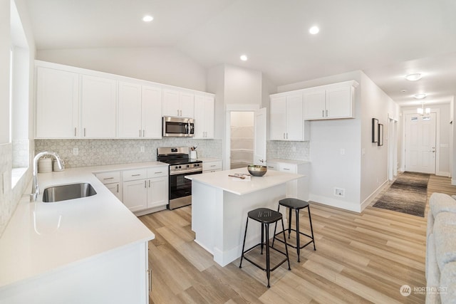 kitchen with appliances with stainless steel finishes, sink, white cabinets, a center island, and lofted ceiling