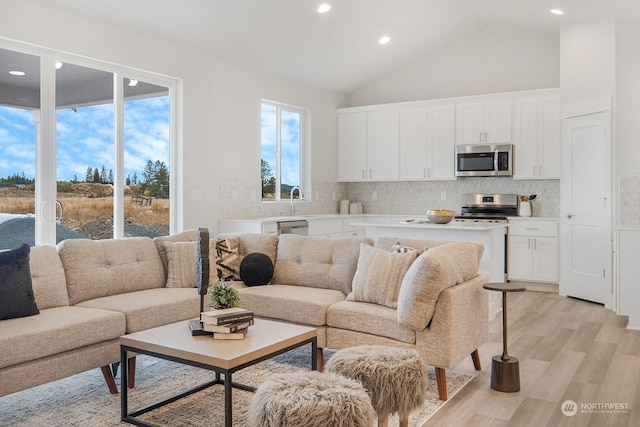 living room with light hardwood / wood-style flooring, high vaulted ceiling, and sink