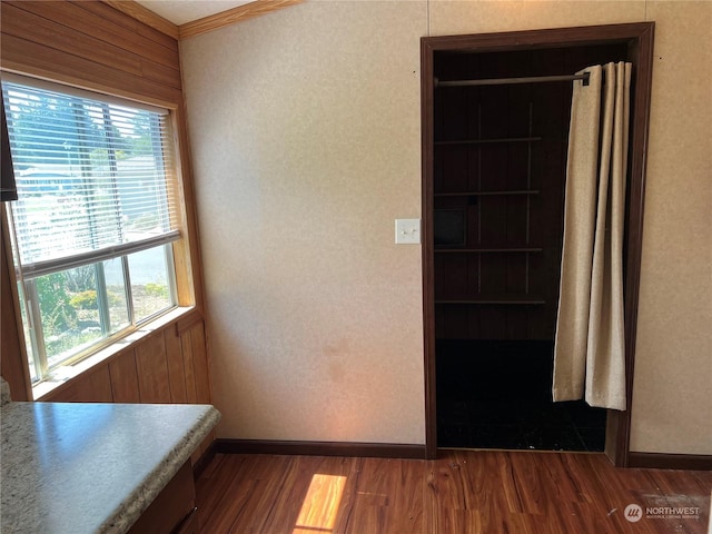 corridor featuring dark hardwood / wood-style floors, wood walls, crown molding, and a wealth of natural light