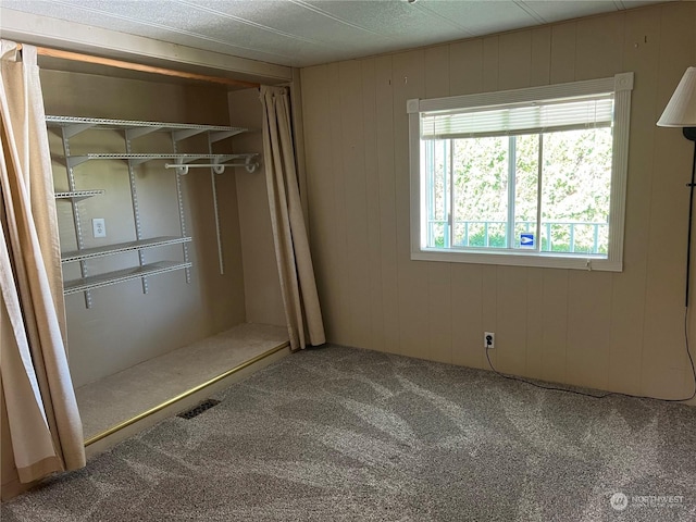 unfurnished bedroom featuring carpet flooring, wood walls, and a closet