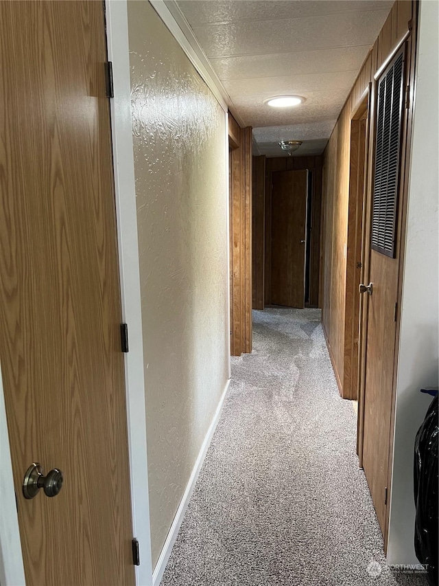 hallway featuring light carpet, a textured ceiling, crown molding, and wood walls