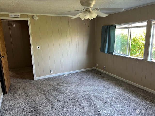 carpeted spare room with ceiling fan, wood walls, and a textured ceiling