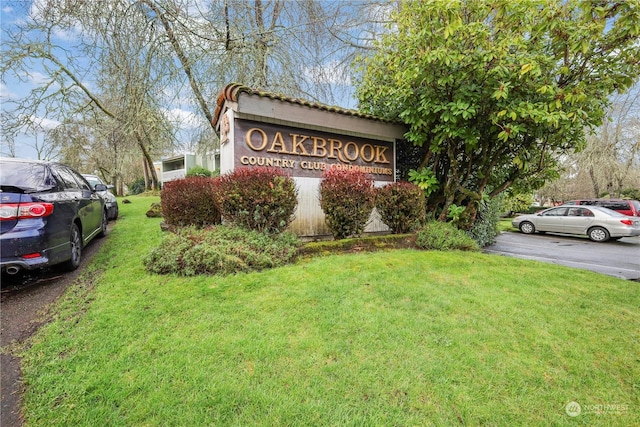 community / neighborhood sign featuring a yard and uncovered parking