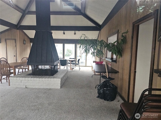 carpeted living room featuring beamed ceiling, wood walls, and high vaulted ceiling