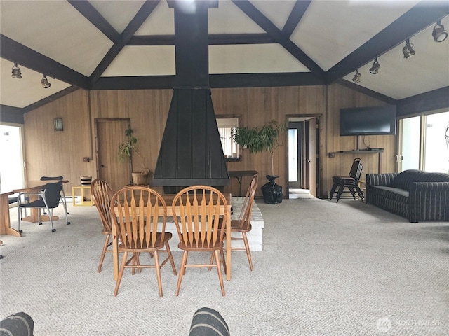 carpeted dining room with track lighting, wood walls, and vaulted ceiling with beams