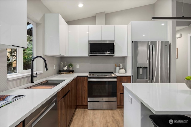 kitchen featuring appliances with stainless steel finishes, tasteful backsplash, sink, white cabinets, and lofted ceiling