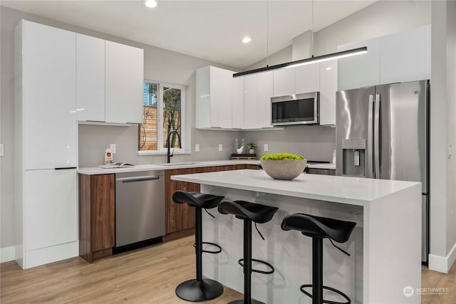 kitchen with white cabinets, stainless steel appliances, vaulted ceiling, and sink