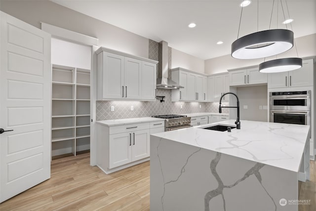 kitchen featuring white cabinets, light stone countertops, sink, and wall chimney exhaust hood