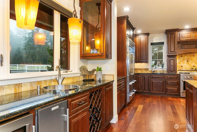 kitchen with dark stone counters, sink, dark wood-type flooring, and premium appliances