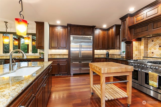 kitchen featuring dark wood-type flooring, high quality appliances, sink, and pendant lighting