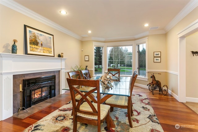 dining room with a tiled fireplace, crown molding, and hardwood / wood-style flooring