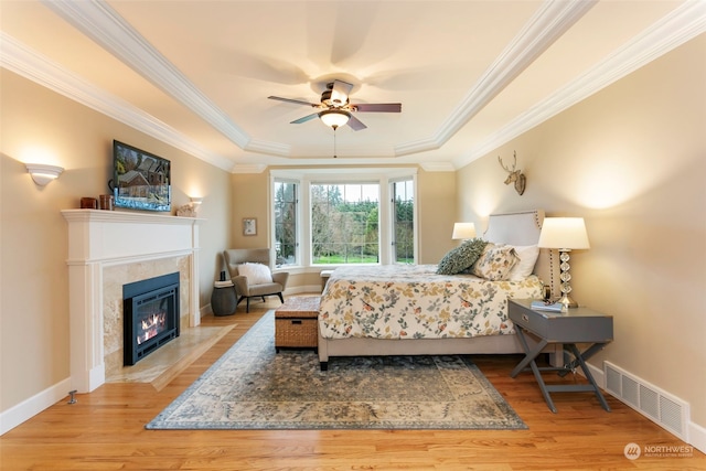 bedroom with a tray ceiling, ceiling fan, crown molding, a tile fireplace, and light hardwood / wood-style floors