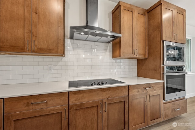 kitchen with wall chimney exhaust hood, stainless steel oven, light hardwood / wood-style flooring, black electric cooktop, and decorative backsplash