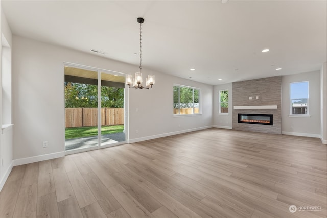 unfurnished living room with a large fireplace, light wood-type flooring, and a chandelier