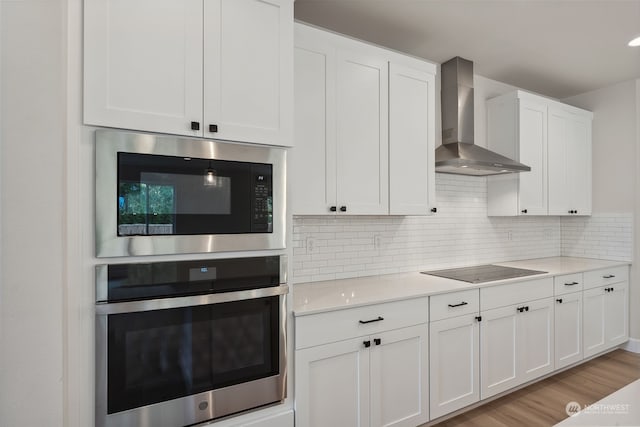 kitchen with white cabinetry, built in microwave, wall chimney exhaust hood, oven, and black electric cooktop