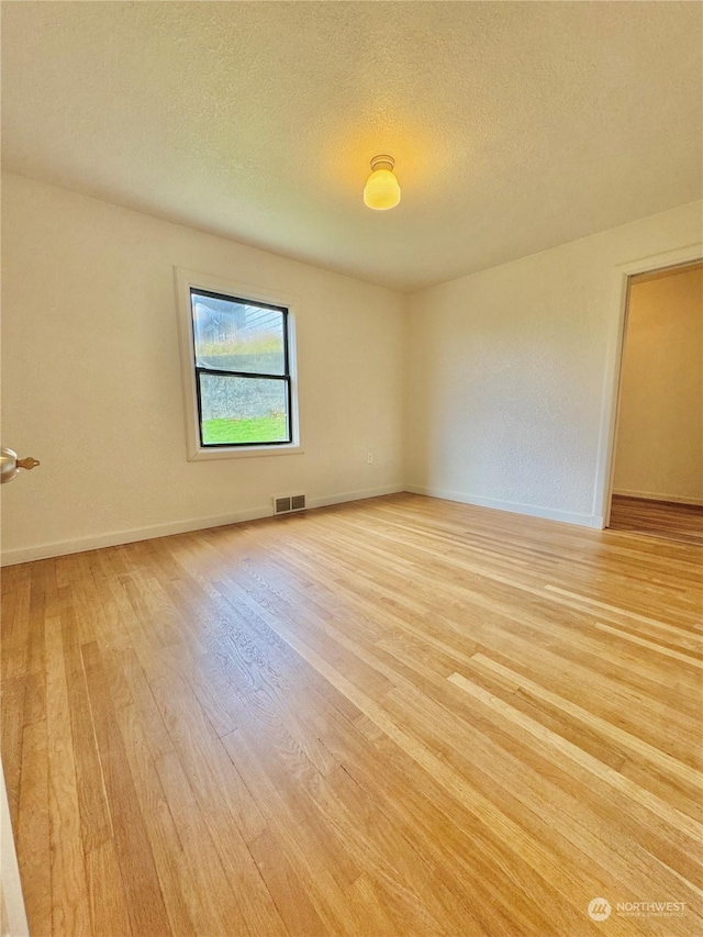 empty room with a textured ceiling and light hardwood / wood-style flooring