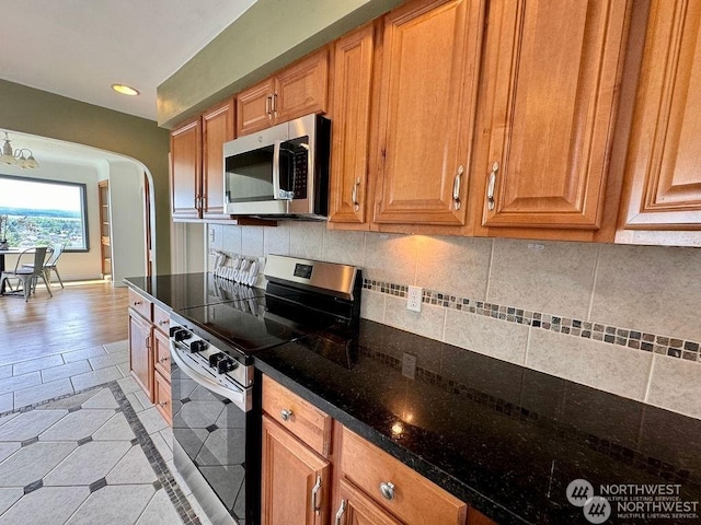 kitchen featuring dark stone countertops, light tile patterned floors, stainless steel appliances, and an inviting chandelier