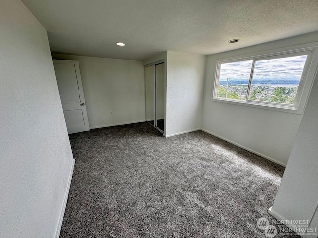 unfurnished bedroom featuring dark carpet, a textured ceiling, and a closet