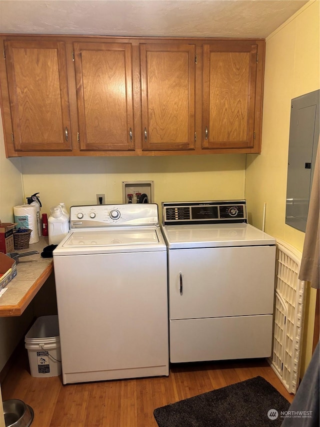 clothes washing area featuring washer and clothes dryer, cabinets, electric panel, and light hardwood / wood-style flooring