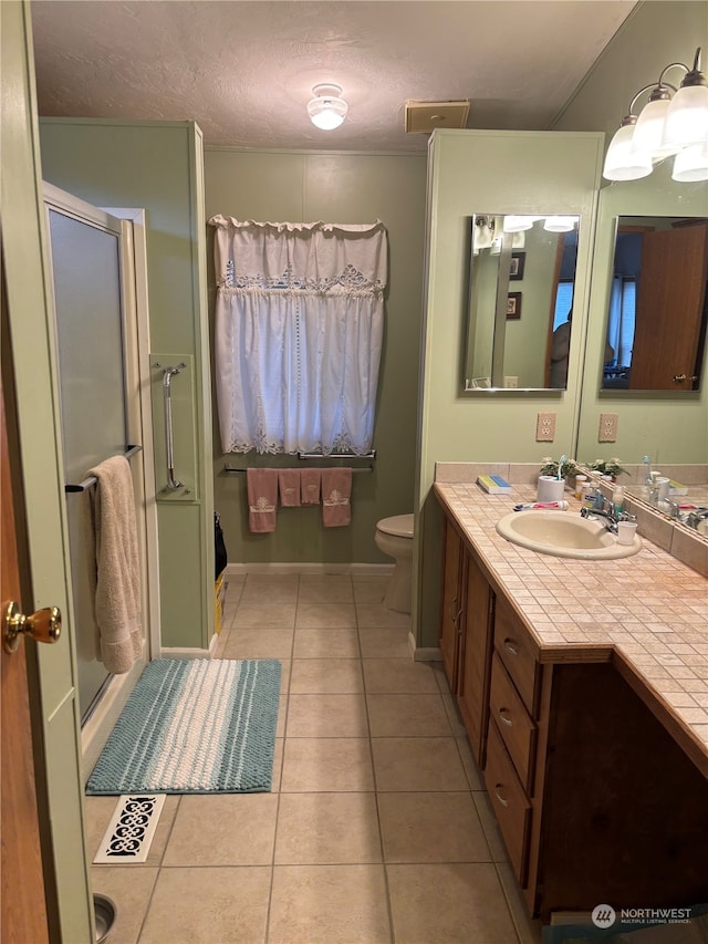 bathroom with walk in shower, a textured ceiling, vanity, tile patterned flooring, and toilet