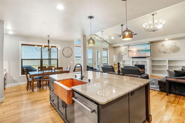 kitchen with sink, stainless steel dishwasher, a premium fireplace, light stone countertops, and a kitchen island with sink