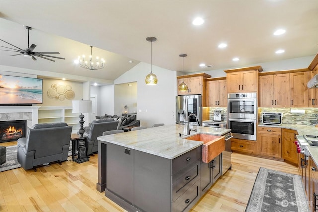 kitchen featuring stainless steel appliances, a large island, a tiled fireplace, decorative backsplash, and hanging light fixtures