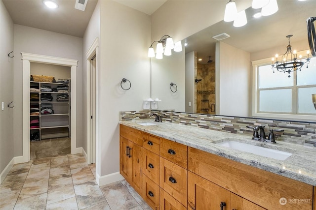 bathroom with a shower with door, vanity, an inviting chandelier, and tasteful backsplash