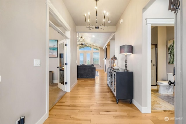 hall with light wood-type flooring, vaulted ceiling, and a notable chandelier