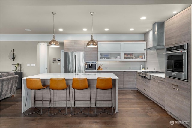 kitchen with stainless steel appliances, a kitchen island with sink, wall chimney exhaust hood, and backsplash