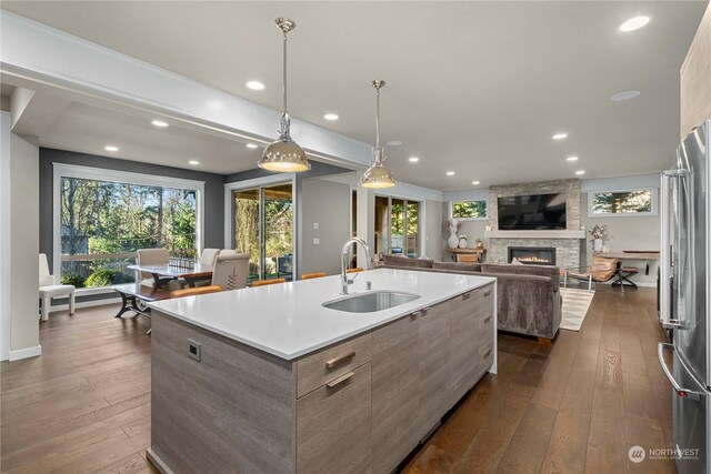 kitchen featuring dark wood-type flooring, high end fridge, sink, and a center island with sink