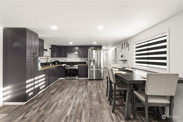 kitchen with decorative backsplash, appliances with stainless steel finishes, dark brown cabinetry, sink, and hardwood / wood-style floors