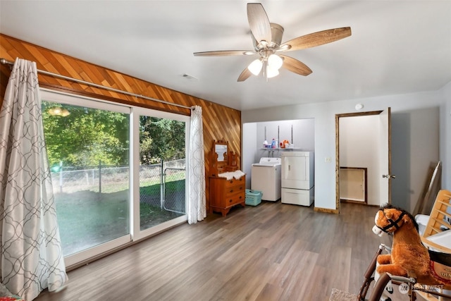 living room featuring ceiling fan, plenty of natural light, wood walls, and washing machine and clothes dryer