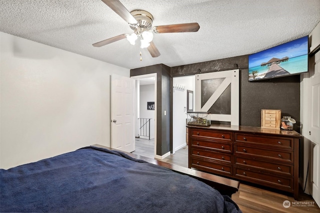 bedroom featuring a textured ceiling, a barn door, ceiling fan, and dark hardwood / wood-style floors