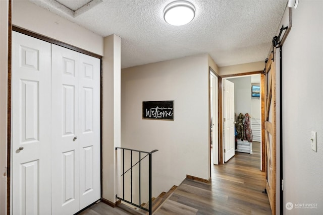 corridor featuring a textured ceiling, a barn door, and dark hardwood / wood-style floors