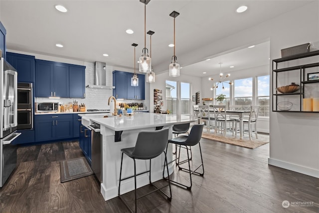 kitchen with a center island with sink, wall chimney exhaust hood, decorative light fixtures, and blue cabinets