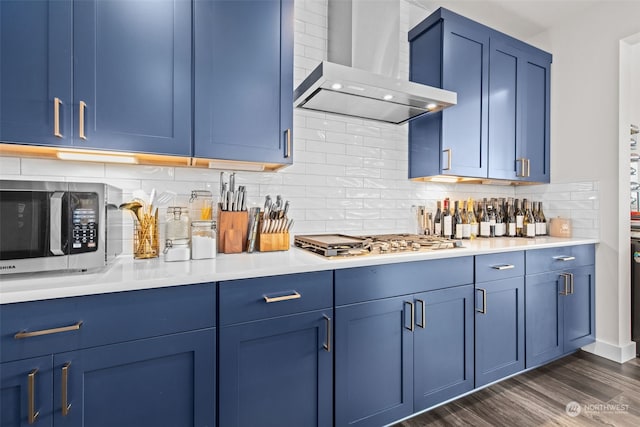 kitchen with tasteful backsplash, stainless steel appliances, blue cabinets, dark wood-type flooring, and wall chimney range hood