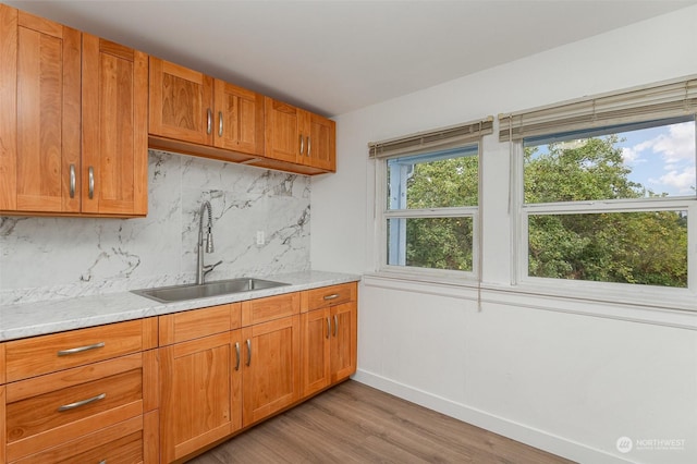 kitchen featuring light stone countertops, light wood-type flooring, sink, and tasteful backsplash