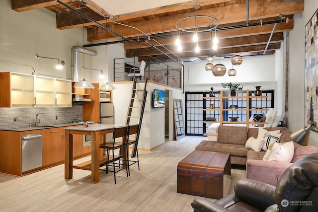 living room featuring beamed ceiling, sink, a high ceiling, and light hardwood / wood-style flooring