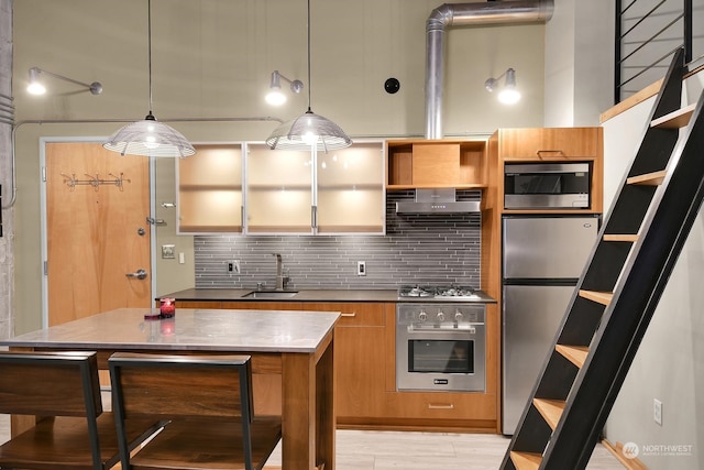 kitchen with hanging light fixtures, sink, appliances with stainless steel finishes, tasteful backsplash, and light hardwood / wood-style floors