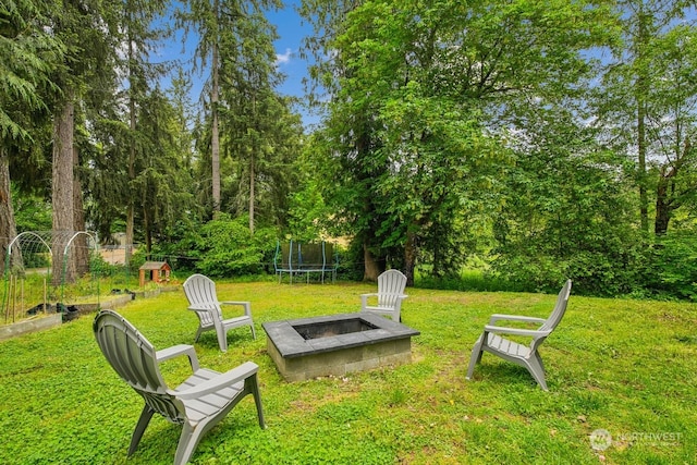 view of community featuring a yard, a trampoline, and an outdoor fire pit