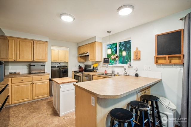 kitchen featuring a kitchen bar, stainless steel appliances, washer and clothes dryer, sink, and a kitchen island