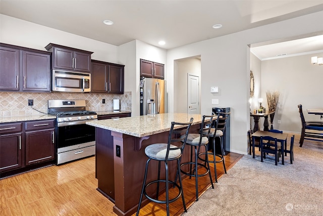 kitchen featuring light stone countertops, stainless steel appliances, a kitchen bar, decorative backsplash, and a kitchen island