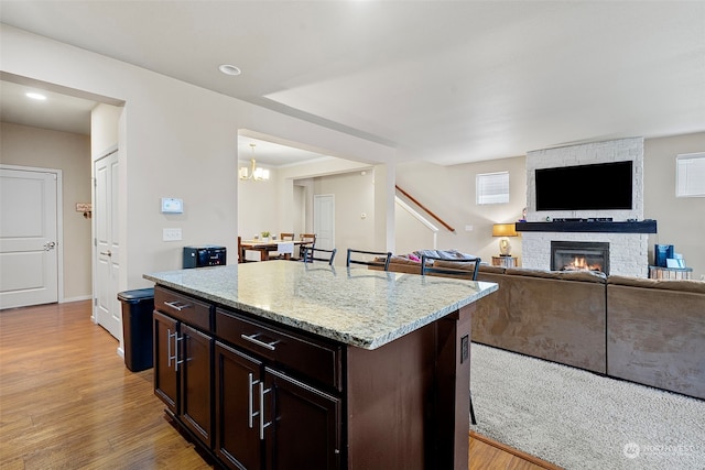 kitchen featuring a center island, a kitchen breakfast bar, light stone countertops, a fireplace, and dark brown cabinets