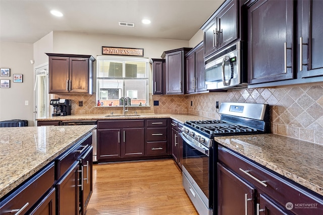 kitchen with light stone countertops, tasteful backsplash, stainless steel appliances, sink, and light hardwood / wood-style floors