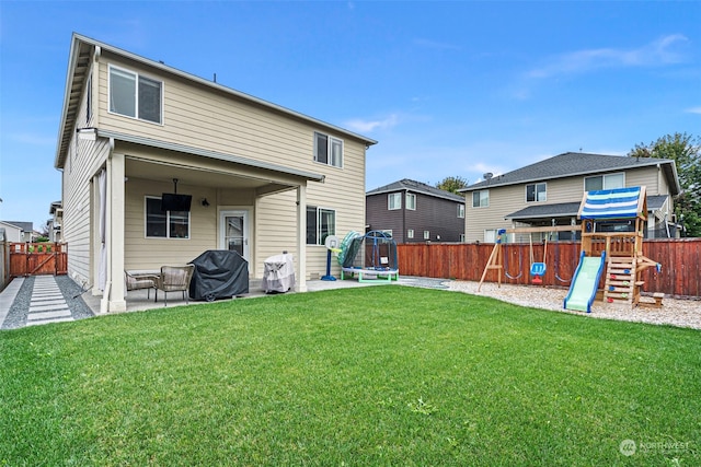 rear view of property with a playground, a yard, a trampoline, and a patio area