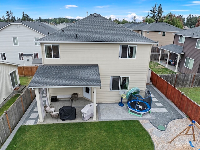 back of property with a trampoline, a patio, and a yard