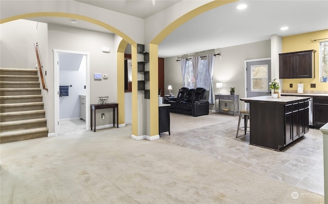 kitchen featuring a kitchen breakfast bar, light colored carpet, dark brown cabinets, and an island with sink