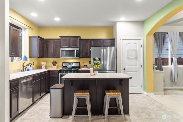 kitchen featuring sink, a kitchen island, a kitchen bar, dark brown cabinetry, and stainless steel appliances