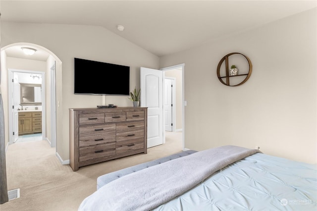 bedroom featuring ensuite bath, light carpet, and lofted ceiling